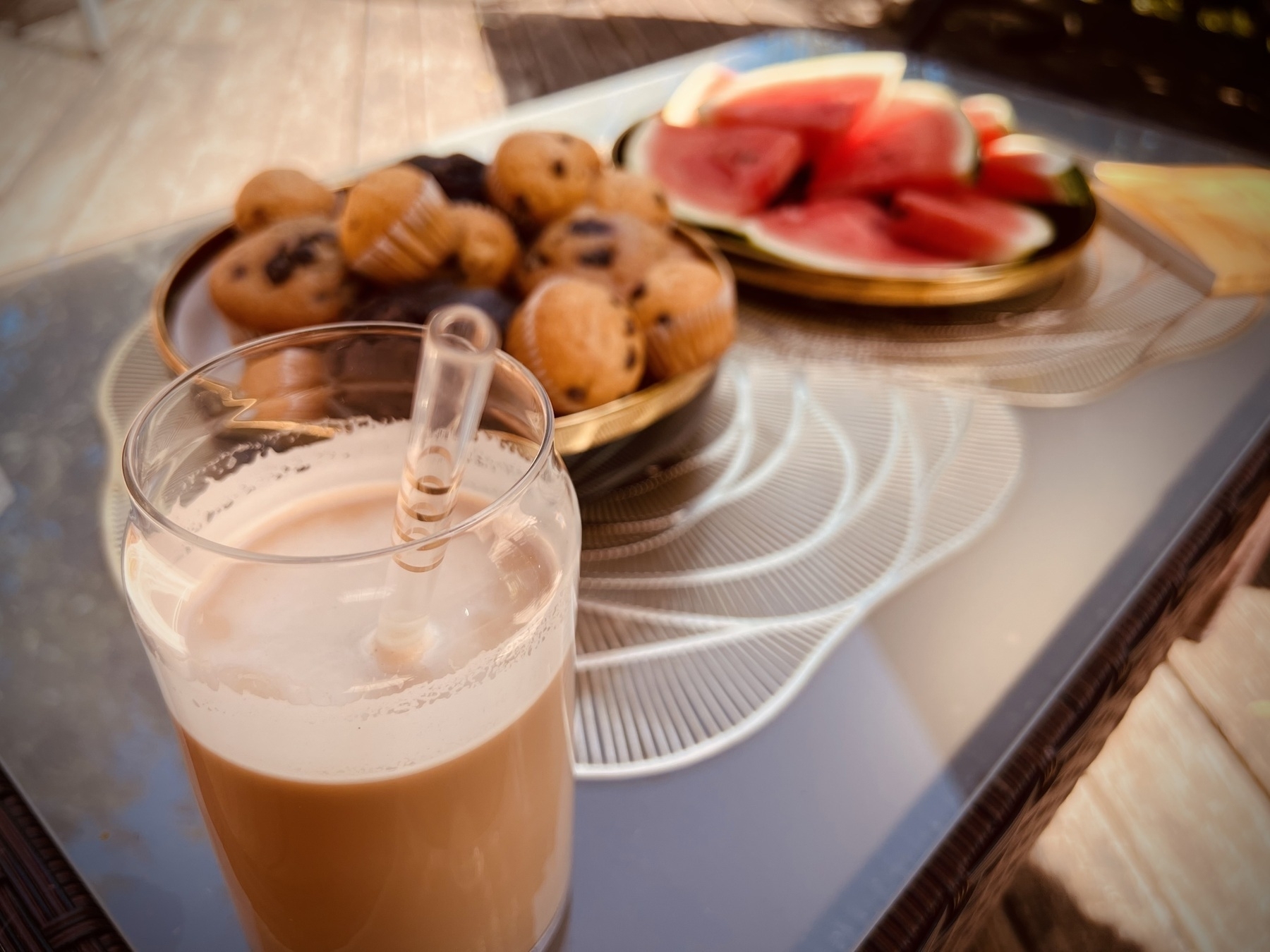 Ein Glas Eiskaffee und im Hintergrund Muffins und Wassermelone. 